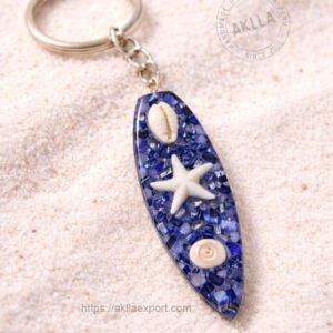 Handmade surfboard keychain in blue resin with resin starfish cowrie shell and spiral shell on white sand